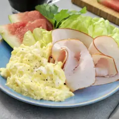 En blå tallrik med äggröra, kalkonpålägg, sallad och vattenmelon. Ett perfekt 5:2 recept för en lätt lunch.