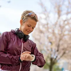 En löpare kollar sin klocka, glad över en bra tid på 5 km. Hon bär hörlurar och löparsolglasögon.