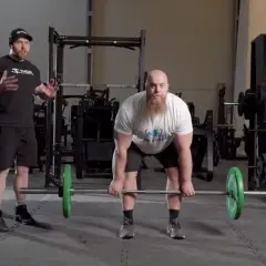 Instruktör visar rdl teknik för en man med skägg som förbereder sig för ett marklyft i ett gym.