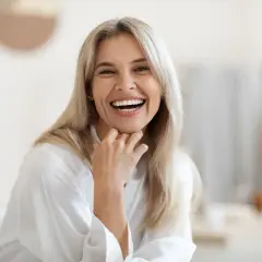 Glad kvinna med blont hår skrattar hjärtligt. Hon har en vit morgonrock och handen vid hakan. Kanske hon funderar på hur kvinnor testosteron påverkar hennes välmående.