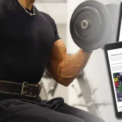 Man med väldefinierade biceps utför en hantelcurl. En surfplatta visar instruktioner för bicepsövningar, inklusive "cable biceps curl".