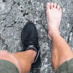 En barfota fot bredvid en barfotasko på en stenig yta. Frågan är om barfotaskor är bra eller dåligt för fötterna.