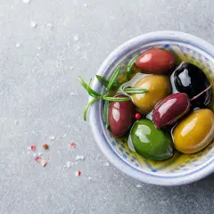 En skål med oliver i olika färger, gröna, röda och svarta, med en rosmarinkvist. Oliver nyttigt och gott!