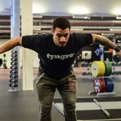 Man tränar baksida axlar med hantlar på gym.