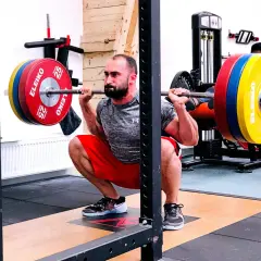 Man utför en djup knäböj med skivstång, en klassisk övning som en del av sin russian squat routine.