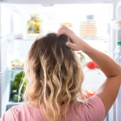 Kvinna kliar sig i huvudet framför ett kylskåp fyllt med mat. Svårt att välja vad som passar en diet på 1500 kalorier per dag.