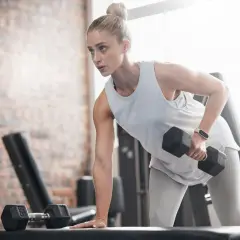 En kvinna med ektomorf kroppstyp tränar rygg med hantlar på ett gym.