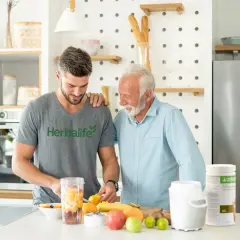 Två män i ett kök förbereder en smoothie med frukt. En burk med proteinpulver står på bänken, perfekt för att få rätt mängd protein per dag.