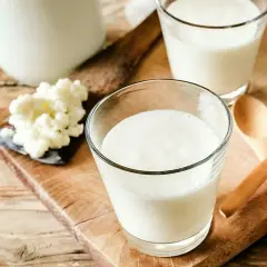 Två glas med krämig kefir står på en träskärbräda. Bredvid syns kefir-kultur och två träskedar. Kefir nyttigt för magen!