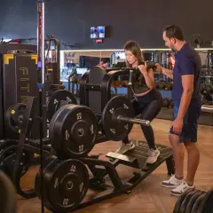 Kvinna utför benpress med instruktör bredvid. En del av ett gym med vikter och maskiner, perfekt för en bro split.