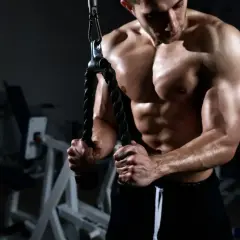 Muskulös man utför triceps pushdown med rep i ett gym.