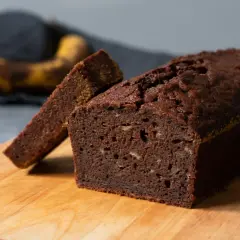 En saftig banankaka utan socker, med en skiva uppskuren. Bakom syns en mogen banan.