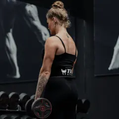 Kvinna med tatueringar utför shrugs med hantlar i ett gym.
