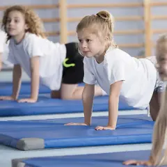 Barn på gympaövning, en aktivitet som motverkar stillasittande barn. De ligger på blåa mattor i en gymnastikhall.