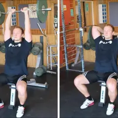 Man utför french press i gym. Han sitter på en bänk och lyfter en skivstång över huvudet.