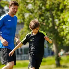 En man och en pojke springer på en gräsmatta, kanske på väg till ett **barn gym** eller en fotbollsträning.