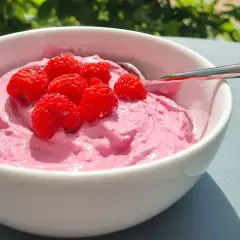 En skål med rosa krämig dessert toppad med färska hallon, perfekt för ett nyttigt fika på jobbet.