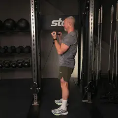 Man utför bicepscurl med stång i ett gym. I bakgrunden syns vikter och träningsutrustning.