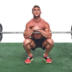 Muskulös man utför en zercher squat med skivstång i armvecken.