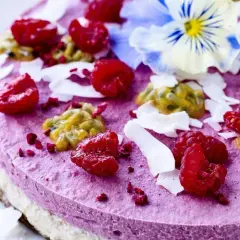 En vacker, lila tårta toppad med hallon, passionsfrukt, kokosflingor och en blå blomma. Perfekt för dig som söker nyttiga kakor.