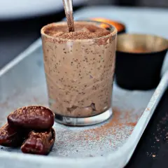 A glass of creamy chia pudding with dates and cocoa powder on a tray.