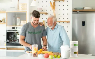 Två män i ett kök förbereder en smoothie med frukt. En burk med proteinpulver står på bänken, perfekt för att få rätt mängd protein per dag.