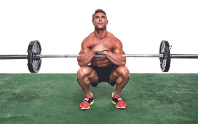 Muskulös man utför en zercher squat med skivstång i armvecken.