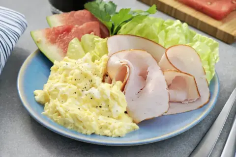 En blå tallrik med äggröra, kalkonpålägg, sallad och vattenmelon. Ett perfekt 5:2 recept för en lätt lunch.