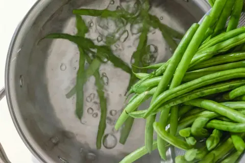 Färska haricots verts kokas i en kastrull. Dessa gröna bönor är nyttiga och en bra källa till vitaminer.