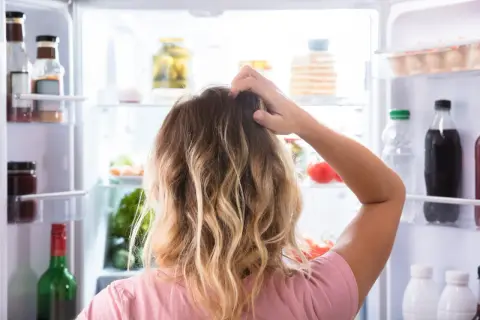 Kvinna kliar sig i huvudet framför ett kylskåp fyllt med mat. Svårt att välja vad som passar en diet på 1500 kalorier per dag.