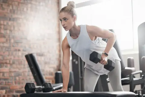 En kvinna med ektomorf kroppstyp tränar rygg med hantlar på ett gym.