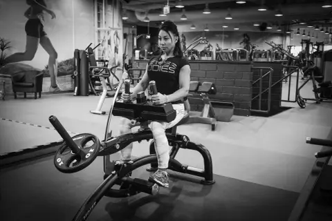 Kvinna tränar vaderna på en sittande vadpress-maskin i ett modernt gym.