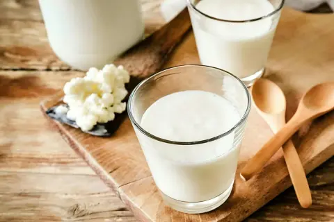 Två glas med krämig kefir står på en träskärbräda. Bredvid syns kefir-kultur och två träskedar. Kefir nyttigt för magen!