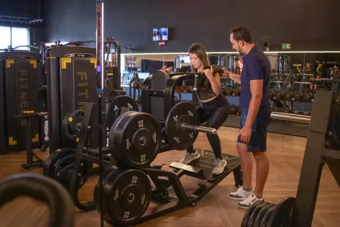 Kvinna utför benpress med instruktör bredvid. En del av ett gym med vikter och maskiner, perfekt för en bro split.