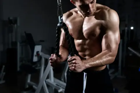 Muskulös man utför triceps pushdown med rep i ett gym.