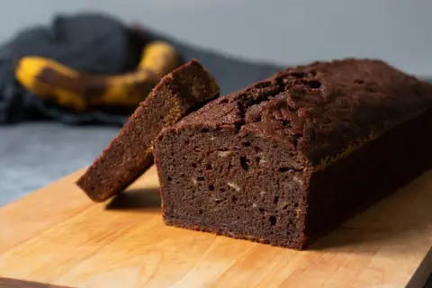 En saftig banankaka utan socker, med en skiva uppskuren. Bakom syns en mogen banan.