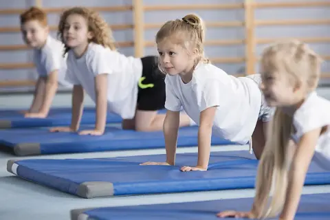 Barn på gympaövning, en aktivitet som motverkar stillasittande barn. De ligger på blåa mattor i en gymnastikhall.