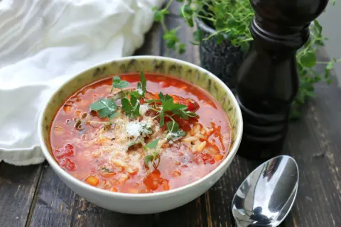 En mustig tomatsoppa med ris och örter, en perfekt källa till vegetariskt protein. Serveras med en sked och pepparkvarn.