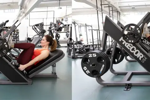 Kvinna tränar benpress i gym. Hon pressar vikter med benen på en Precor-maskin.