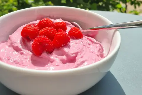 En skål med rosa krämig dessert toppad med färska hallon, perfekt för ett nyttigt fika på jobbet.