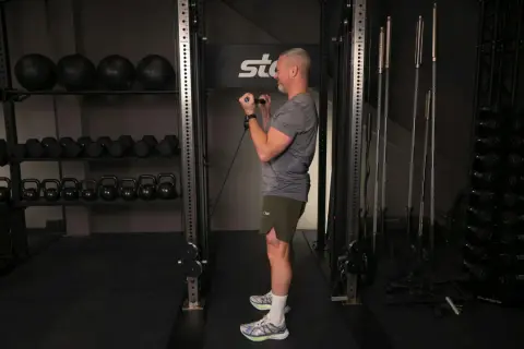 Man utför bicepscurl med stång i ett gym. I bakgrunden syns vikter och träningsutrustning.