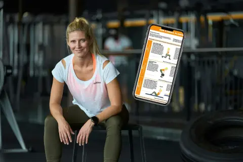 En kvinna sitter i ett gym med en telefon som visar en träningsplan. Hon ser ut att veta hur man blir stark.
