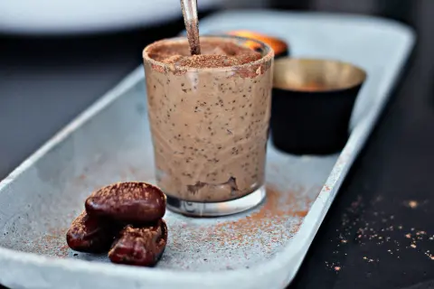 A glass of creamy chia pudding with dates and cocoa powder on a tray.