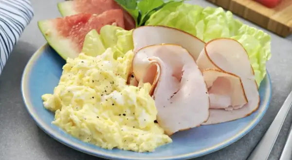 En blå tallrik med äggröra, kalkonpålägg, sallad och vattenmelon. Ett perfekt 5:2 recept för en lätt lunch.