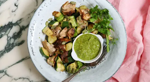 En tallrik med kyckling, zucchini och pumpafrön, serverad med en grön sås. En perfekt snabb nyttig lunch för en solig dag.