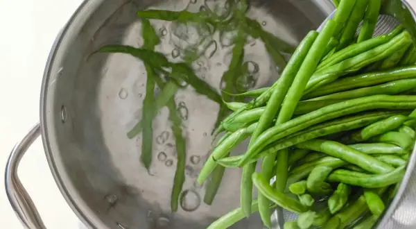 Färska haricots verts kokas i en kastrull. Dessa gröna bönor är nyttiga och en bra källa till vitaminer.