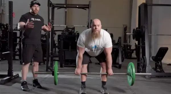 Instruktör visar rdl teknik för en man med skägg som förbereder sig för ett marklyft i ett gym.