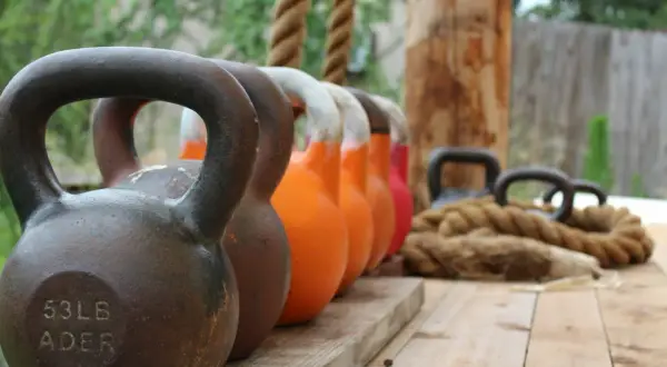 En rad kettlebells i olika färger och vikter, redo för nya reps och set. Ett rep ligger bredvid, redo för träning.
