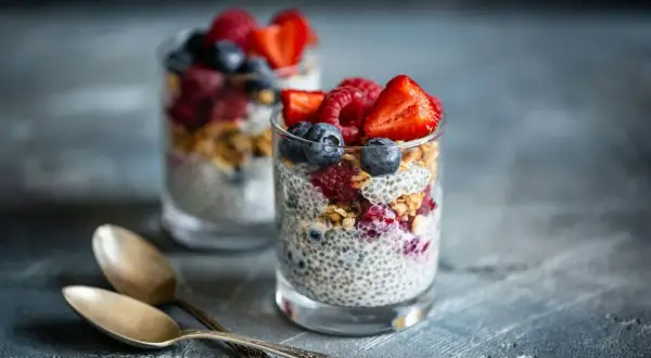 Två glas med chiapudding, toppad med bär och granola. Perfekt för en hälsosam frukost med koll på chiapudding kalorier.