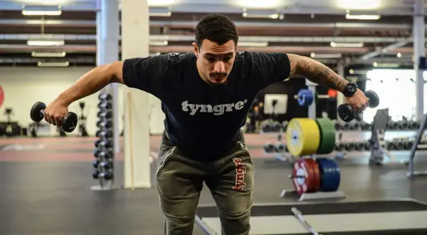 Man tränar baksida axlar med hantlar på gym.